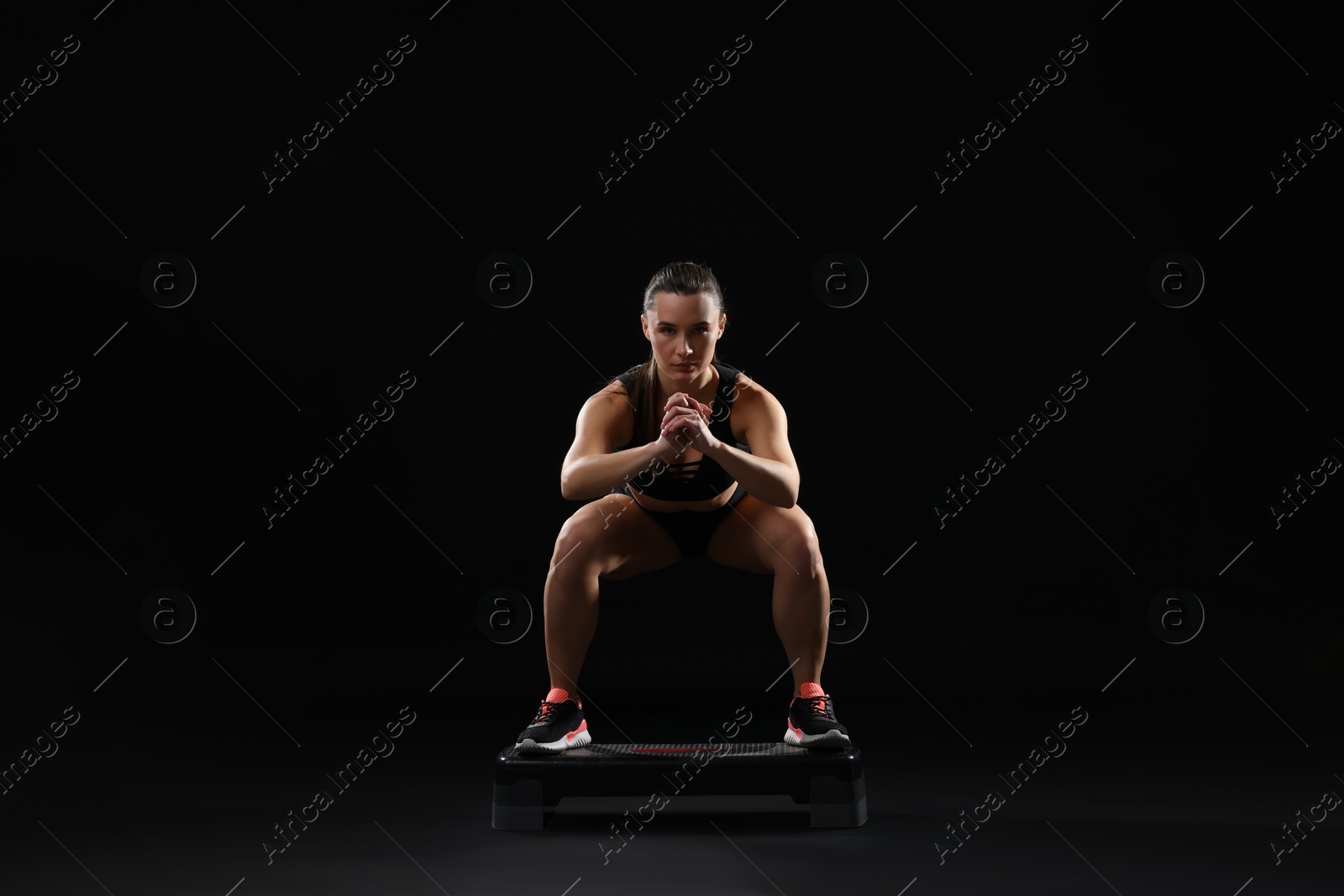 Photo of Beautiful woman in sportswear training on black background