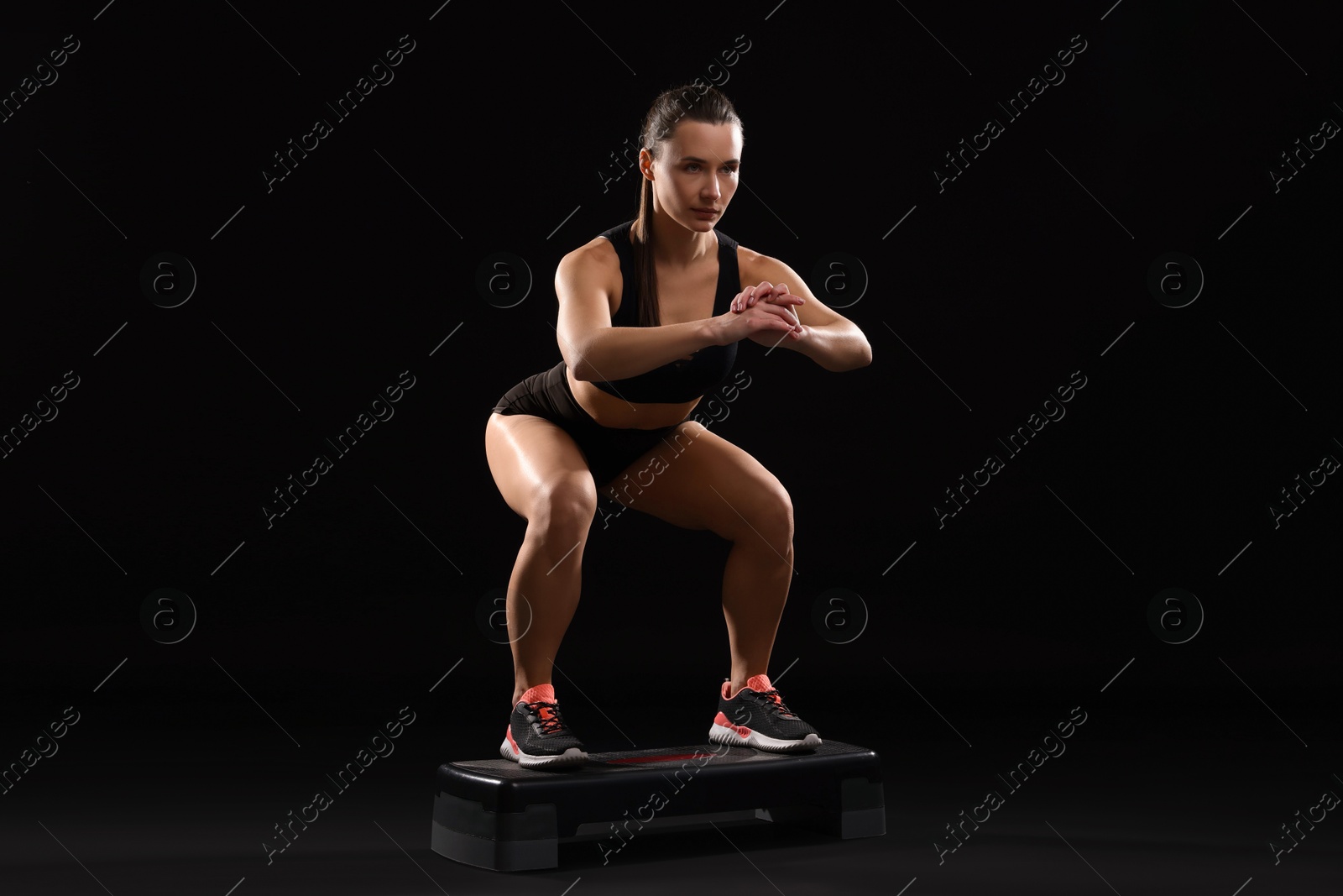 Photo of Beautiful woman in sportswear training on black background