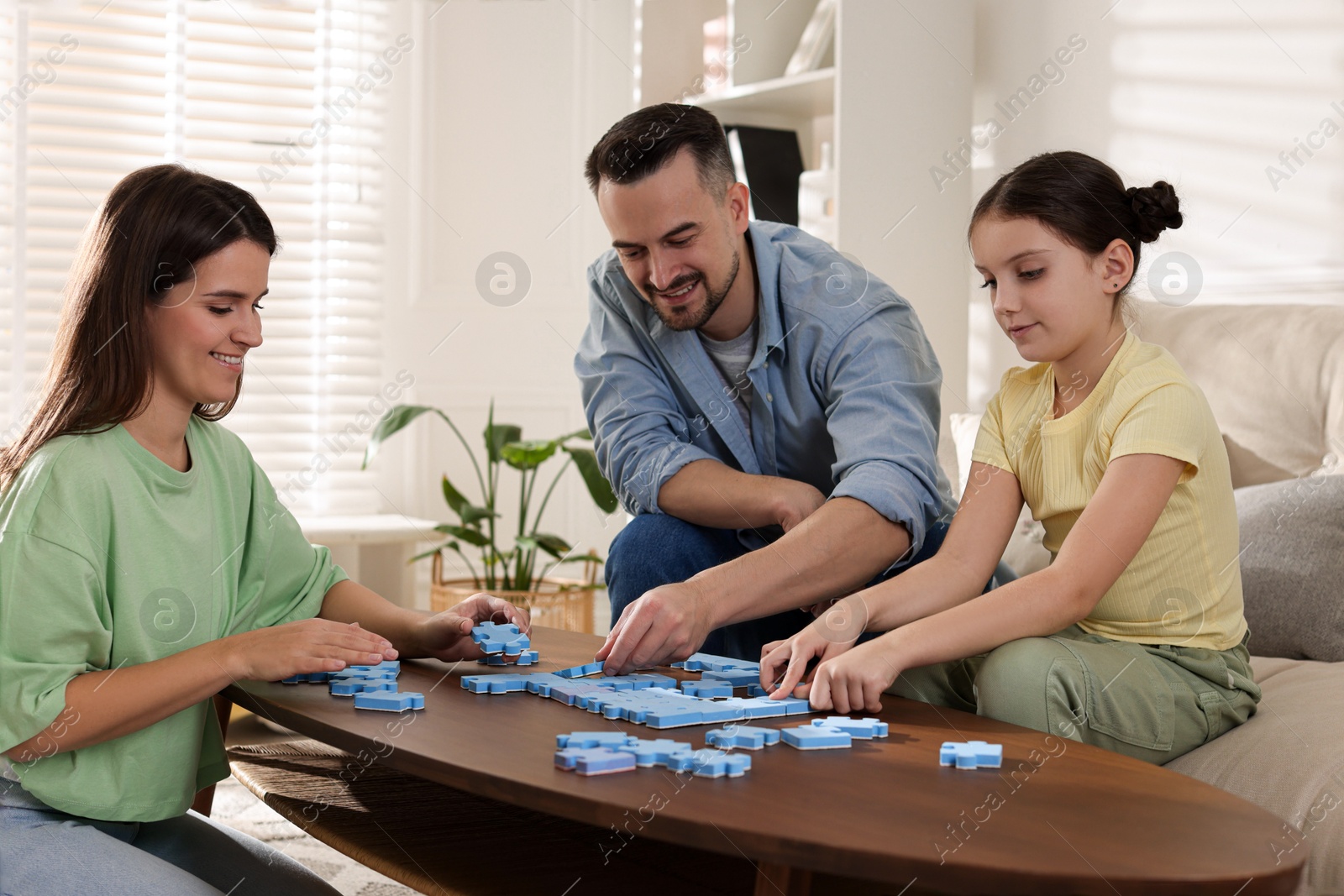 Photo of Happy parents and their daughter solving puzzle together at wooden table indoors