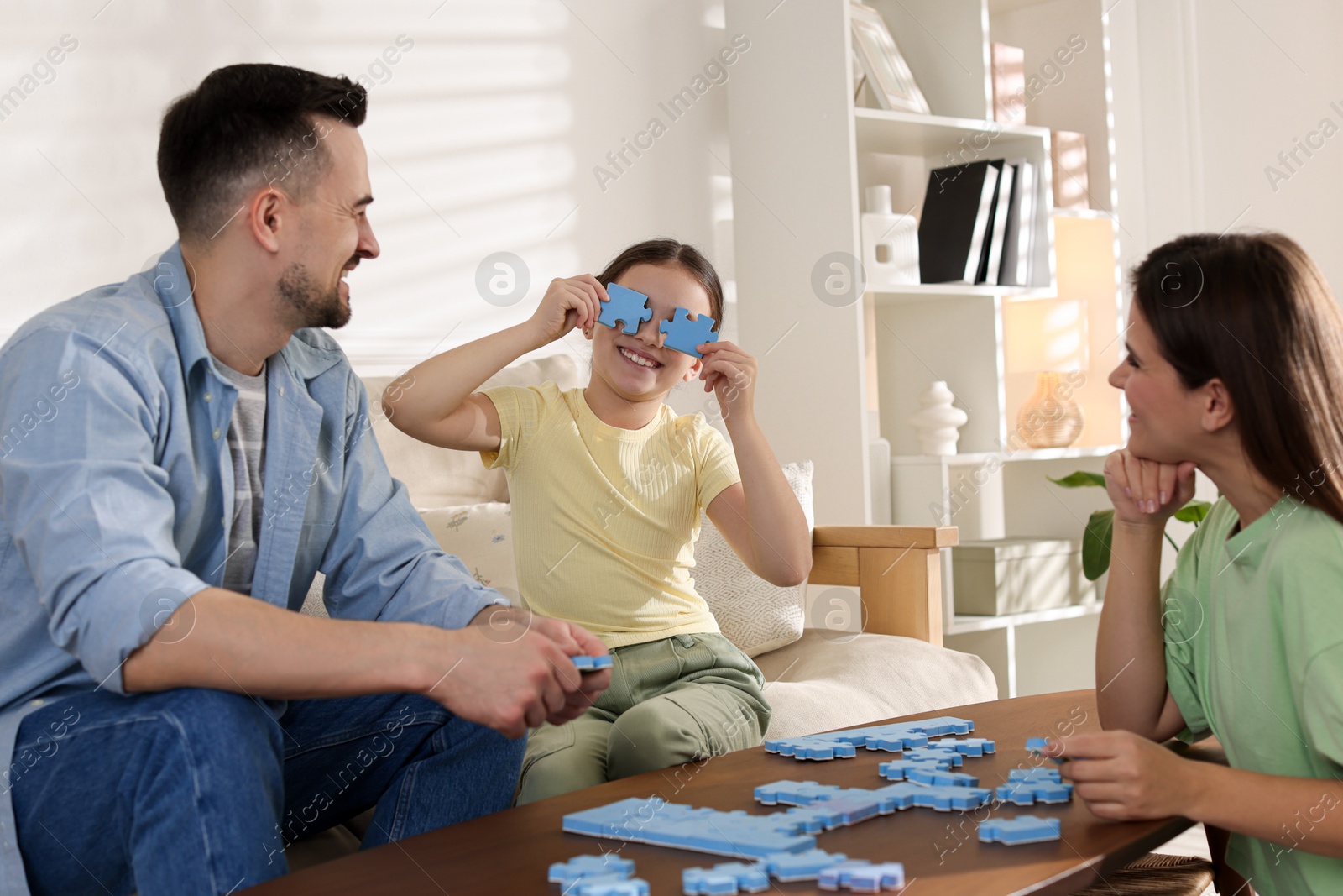 Photo of Happy parents and their daughter solving puzzle together at wooden table indoors