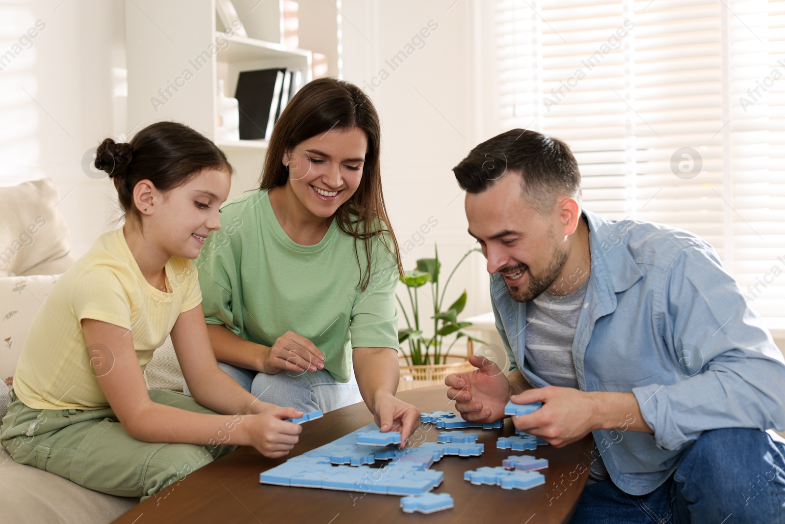 Photo of Happy parents and their daughter solving puzzle together at wooden table indoors