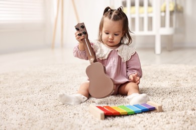 Photo of Cute little girl playing with toy guitar on floor at home