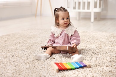 Photo of Cute little girl playing with toy guitar on floor at home