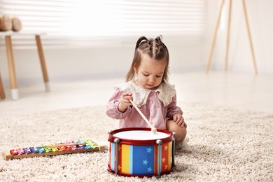 Photo of Cute little girl playing with toy drum and drumstick on floor at home