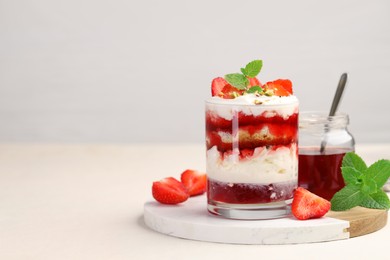 Photo of Tasty trifle dessert. Strawberries, sponge cake and whipped cream in glass on beige table, space for text