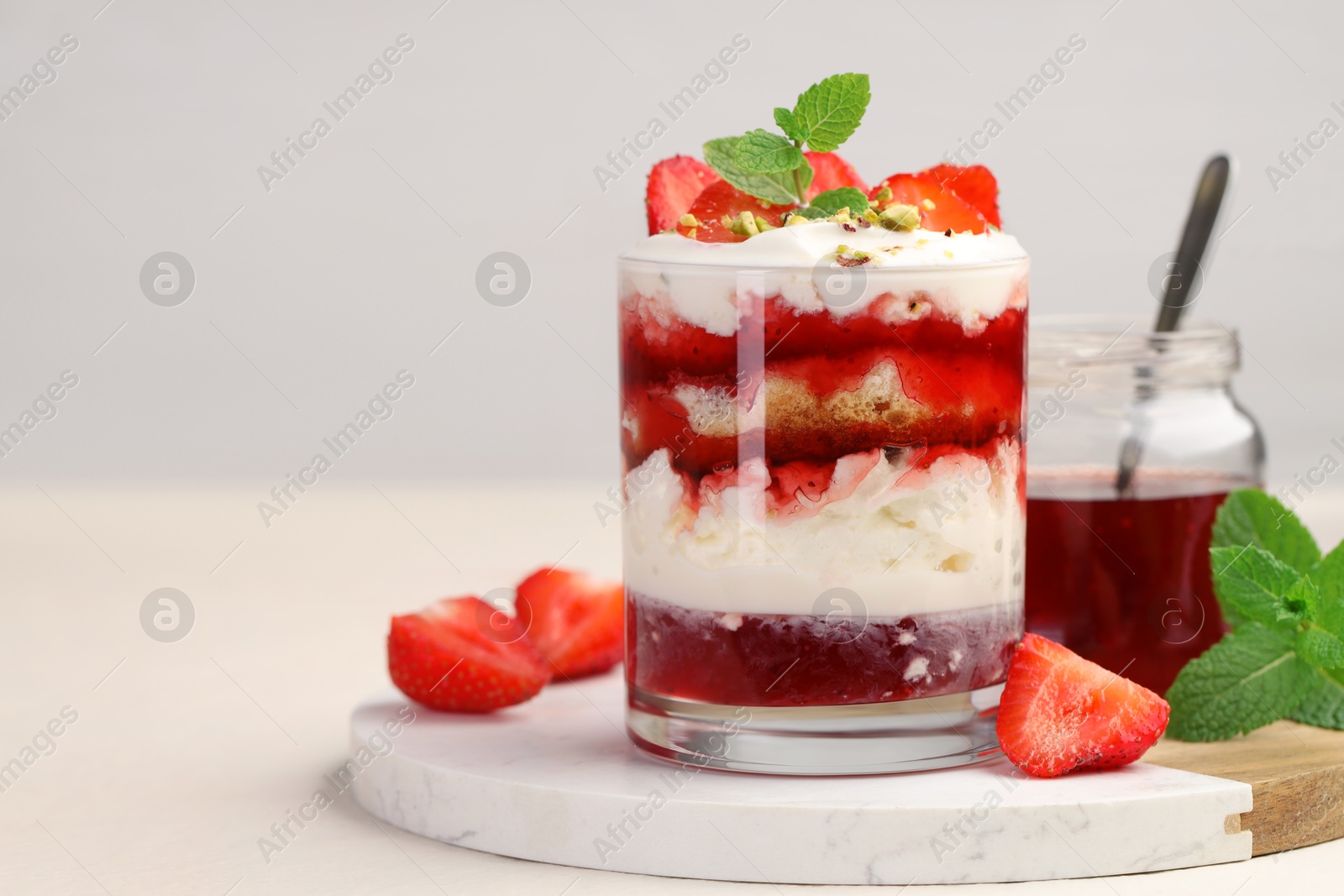 Photo of Tasty trifle dessert. Strawberries, sponge cake and whipped cream in glass on beige table, space for text