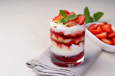 Photo of Tasty trifle dessert. Strawberries, sponge cake and whipped cream in glass on beige table, space for text