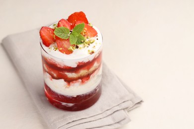 Photo of Tasty trifle dessert. Strawberries, sponge cake and whipped cream in glass on beige table, space for text