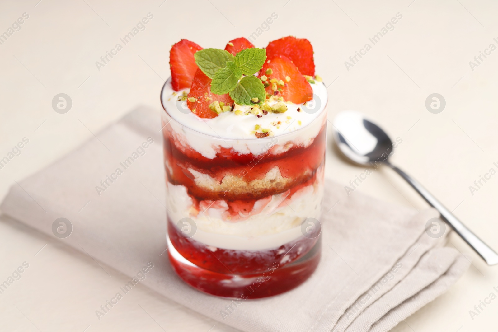 Photo of Tasty trifle dessert. Strawberries, sponge cake and whipped cream in glass on beige table