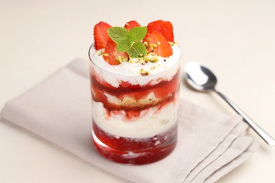 Photo of Tasty trifle dessert. Strawberries, sponge cake and whipped cream in glass on beige table