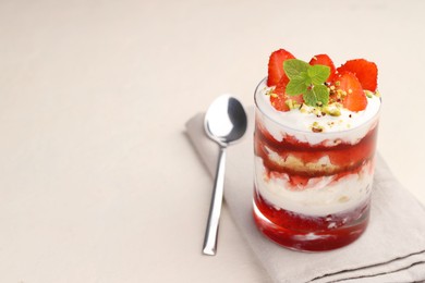 Photo of Tasty trifle dessert. Strawberries, sponge cake and whipped cream in glass on beige table, space for text