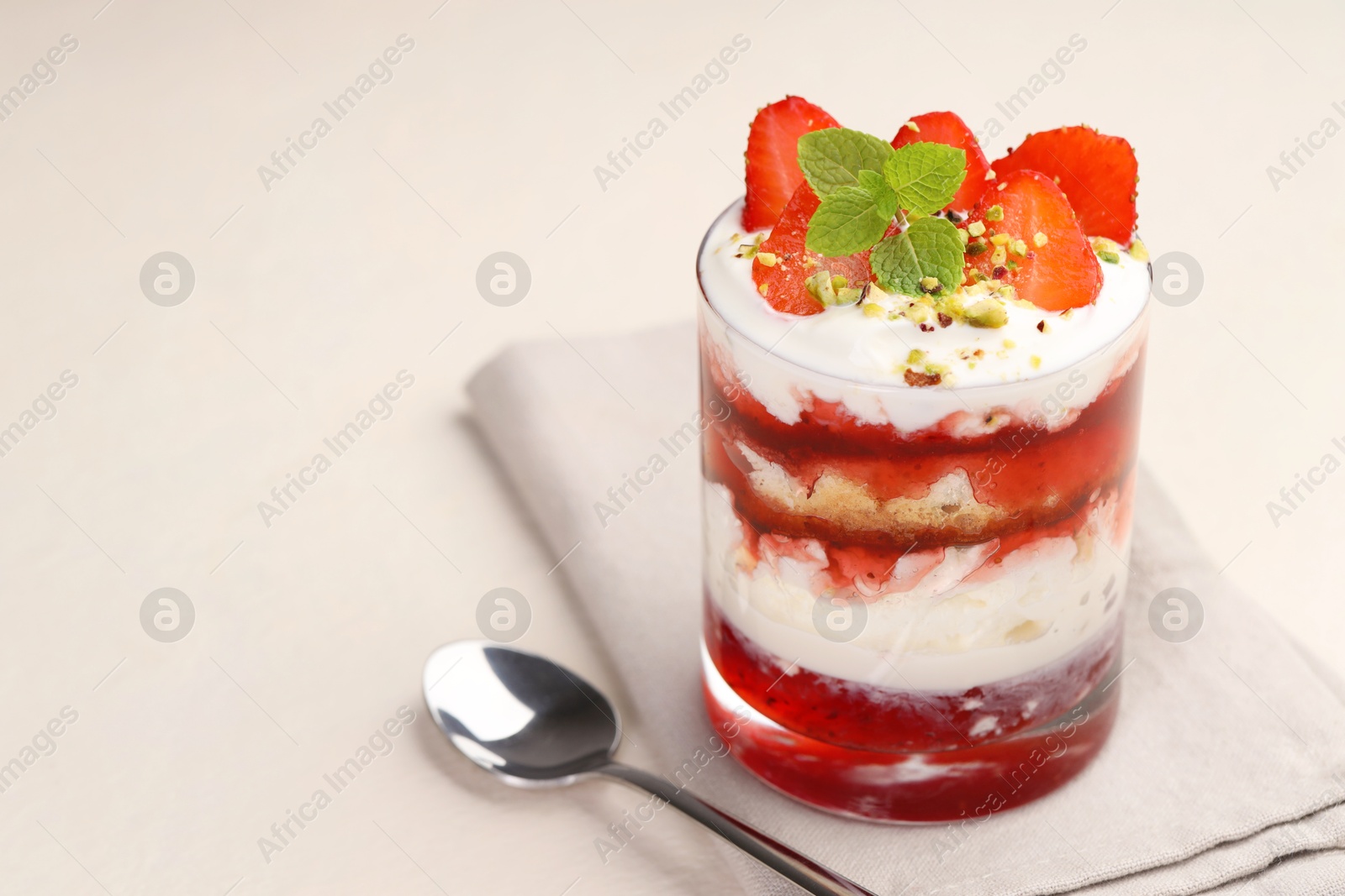 Photo of Tasty trifle dessert. Strawberries, sponge cake and whipped cream in glass on beige table, space for text