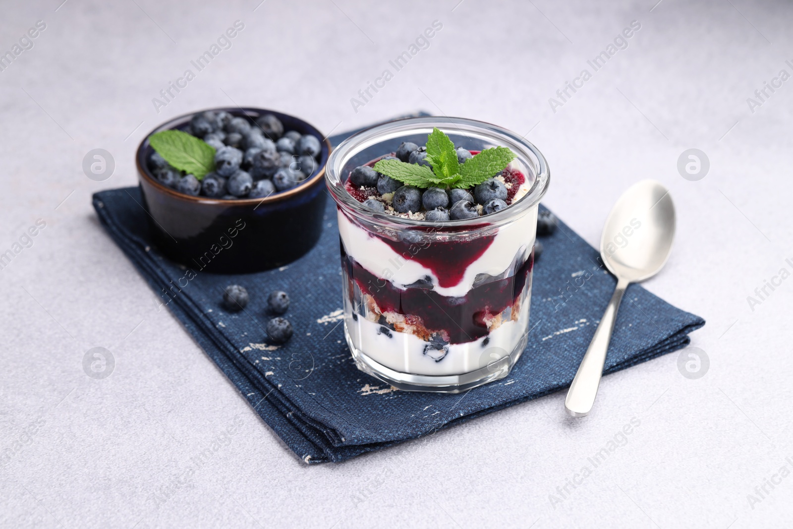 Photo of Tasty trifle dessert. Blueberries, sponge cake and whipped cream in glass on light grey table