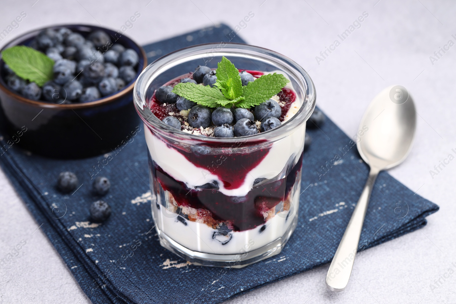 Photo of Tasty trifle dessert. Blueberries, sponge cake and whipped cream in glass on light grey table