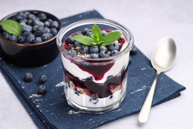 Photo of Tasty trifle dessert. Blueberries, sponge cake and whipped cream in glass on light grey table