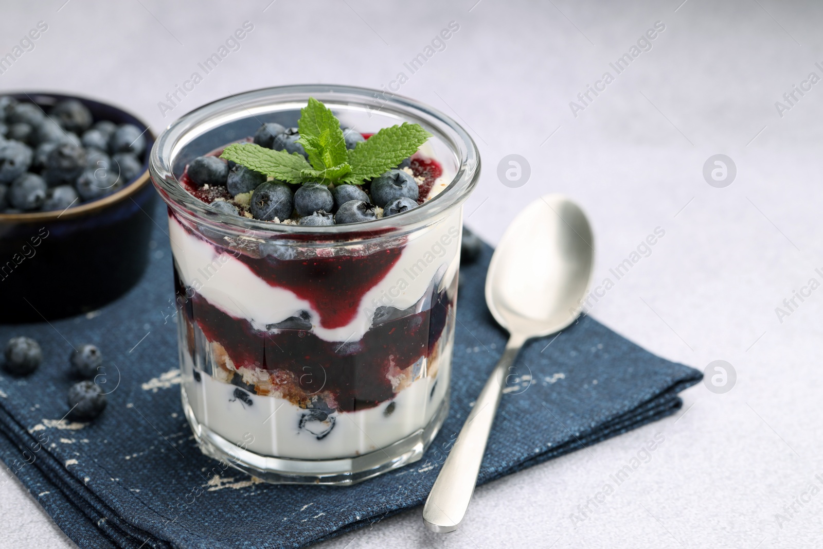 Photo of Tasty trifle dessert. Blueberries, sponge cake and whipped cream in glass on light grey table