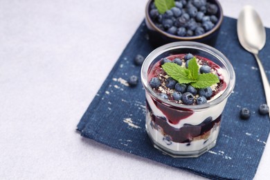 Photo of Tasty trifle dessert. Blueberries, sponge cake and whipped cream in glass on light grey table, space for text