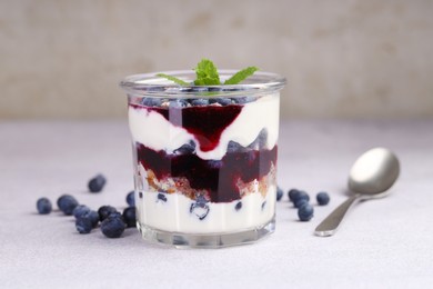 Photo of Tasty trifle dessert. Blueberries, sponge cake and whipped cream in glass on light grey table