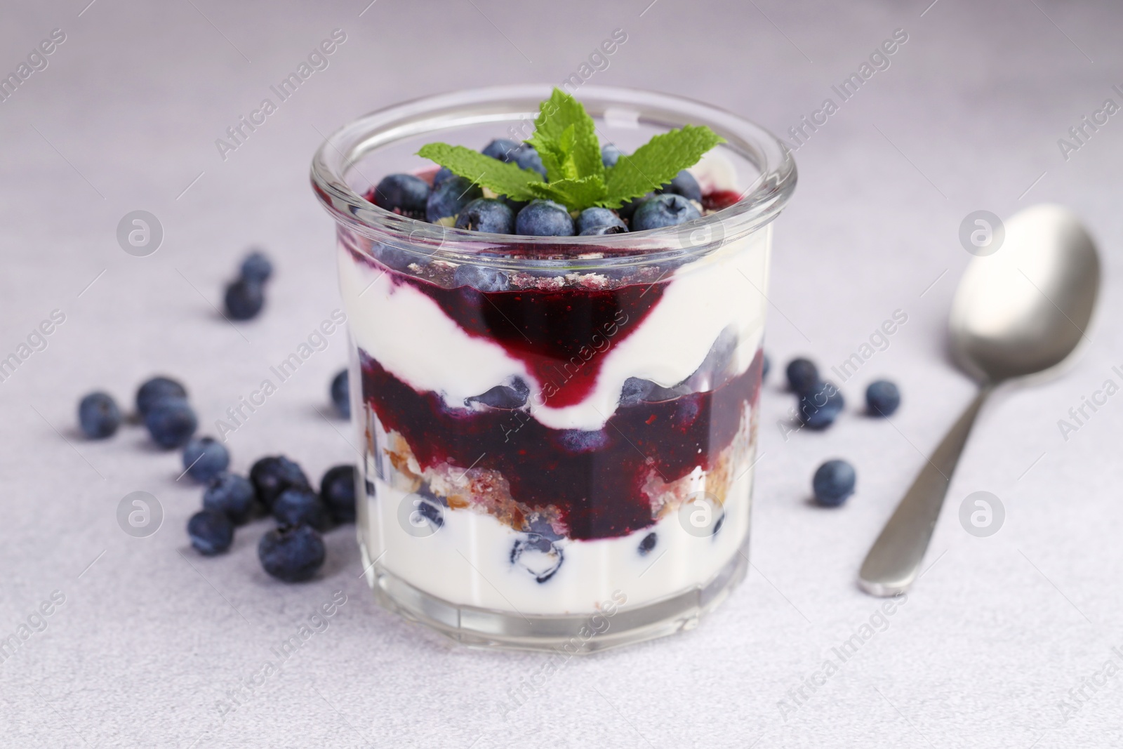 Photo of Tasty trifle dessert. Blueberries, sponge cake and whipped cream in glass on light grey table