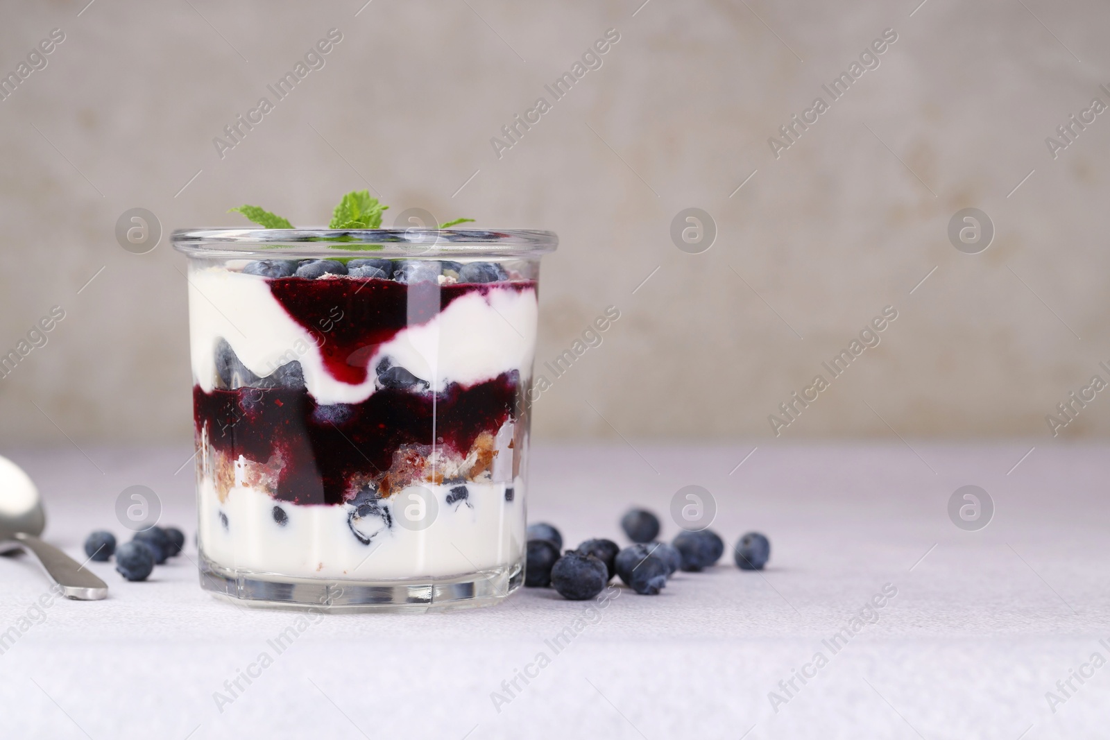 Photo of Tasty trifle dessert. Blueberries, sponge cake and whipped cream in glass on light grey table, space for text