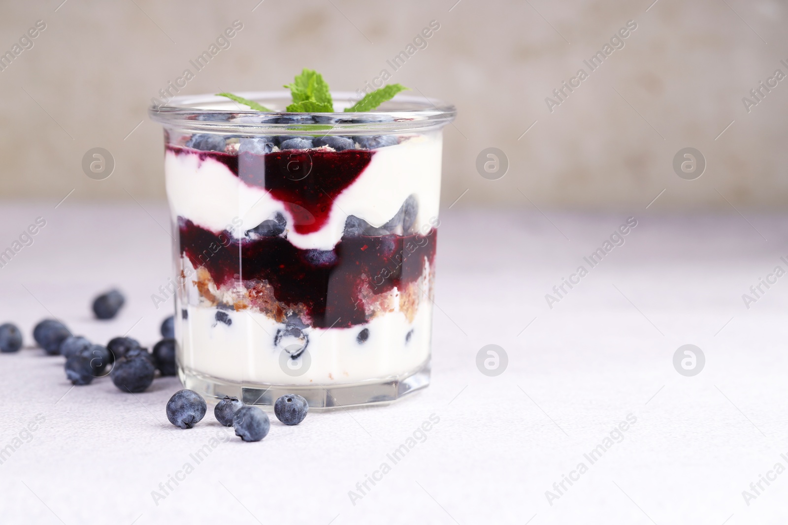 Photo of Tasty trifle dessert. Blueberries, sponge cake and whipped cream in glass on light grey table, space for text