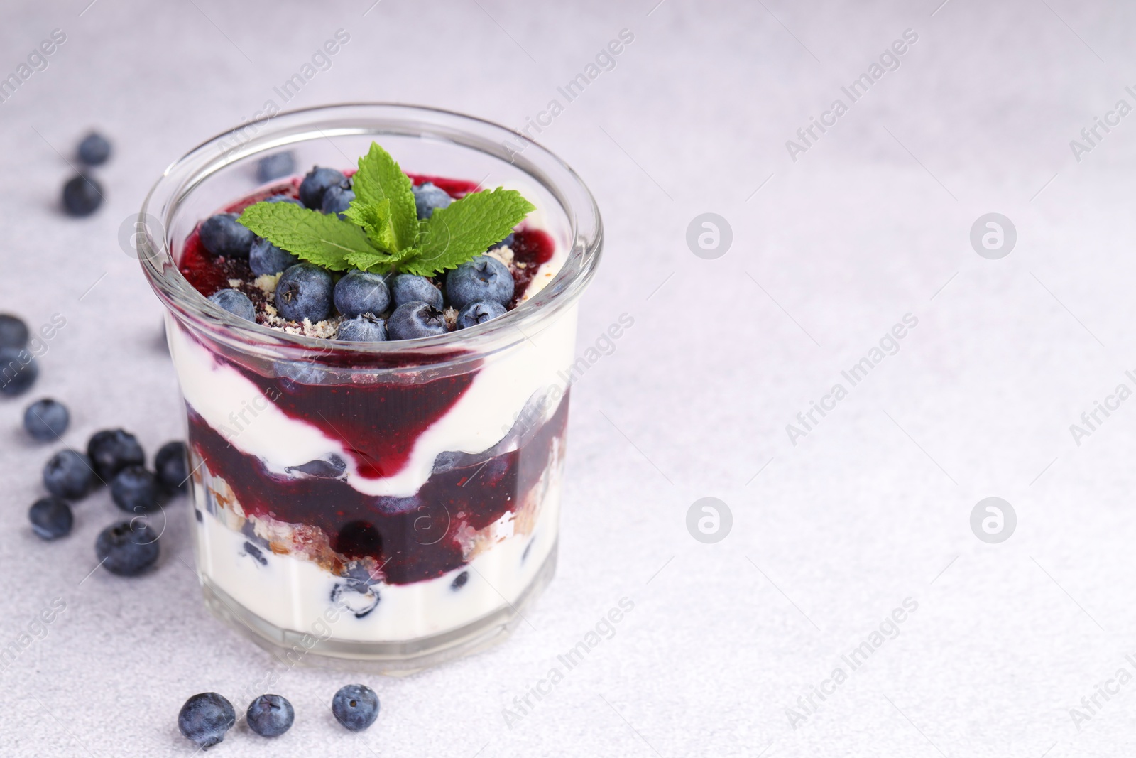 Photo of Tasty trifle dessert. Blueberries, sponge cake and whipped cream in glass on light grey table, space for text