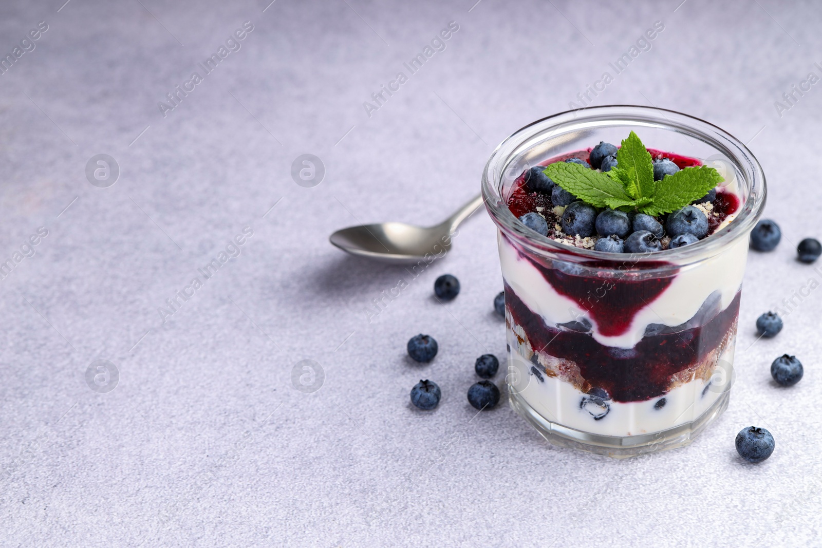 Photo of Tasty trifle dessert. Blueberries, sponge cake and whipped cream in glass on light grey table, space for text