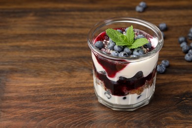 Photo of Tasty trifle dessert. Blueberries, sponge cake and whipped cream in glass on wooden table, space for text