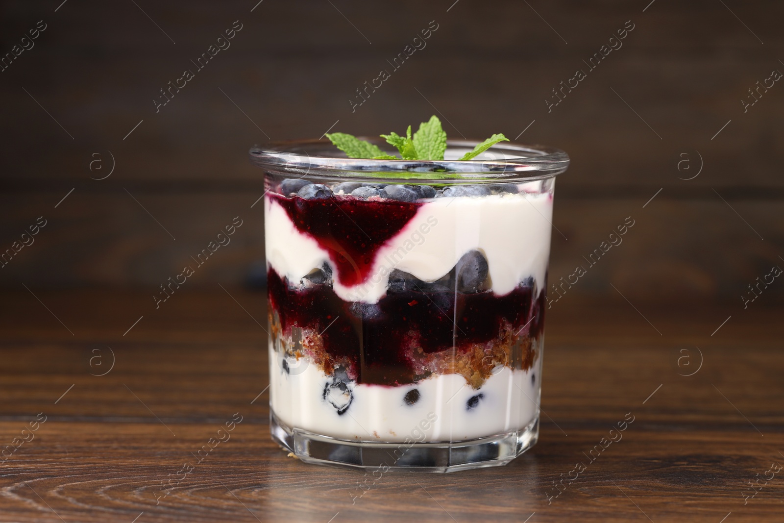 Photo of Tasty trifle dessert. Blueberries, sponge cake and whipped cream in glass on wooden table