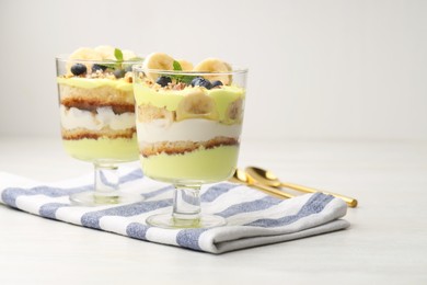 Photo of Tasty trifle dessert. Banana, blueberries, sponge cake and whipped cream in glasses on white wooden table, space for text