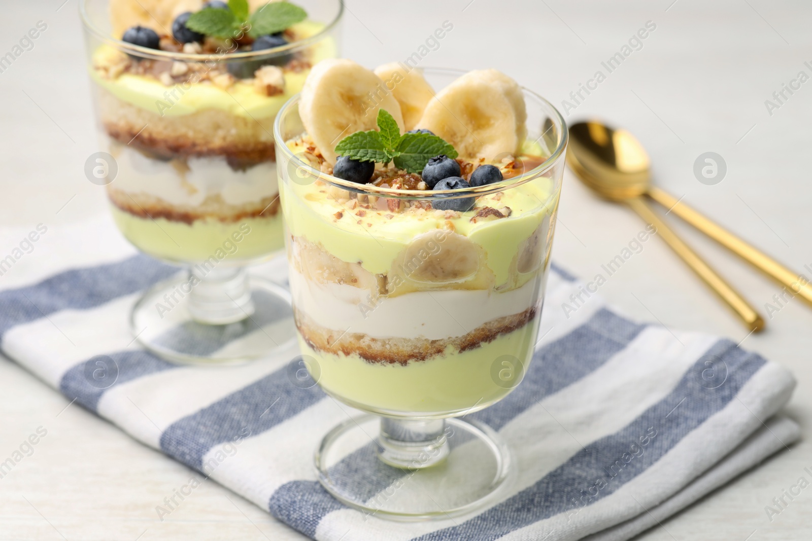 Photo of Tasty trifle dessert. Banana, blueberries, sponge cake and whipped cream in glasses on white wooden table