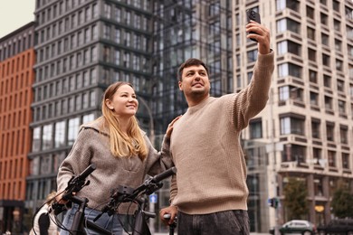 Photo of Beautiful happy couple with bicycles taking selfie outdoors