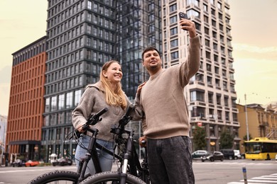 Photo of Beautiful happy couple with bicycles taking selfie outdoors