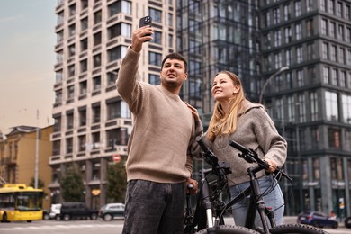 Photo of Beautiful happy couple with bicycles taking selfie outdoors