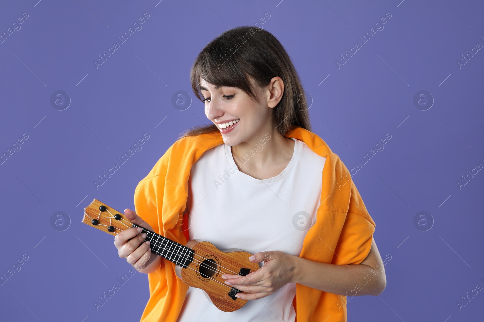 Photo of Happy woman playing ukulele on purple background