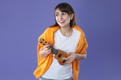 Photo of Happy woman playing ukulele on purple background, space for text