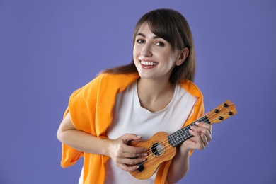 Photo of Happy woman playing ukulele on purple background