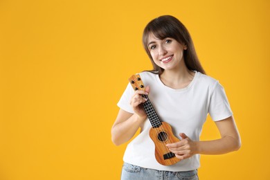 Photo of Happy woman playing ukulele on orange background, space for text