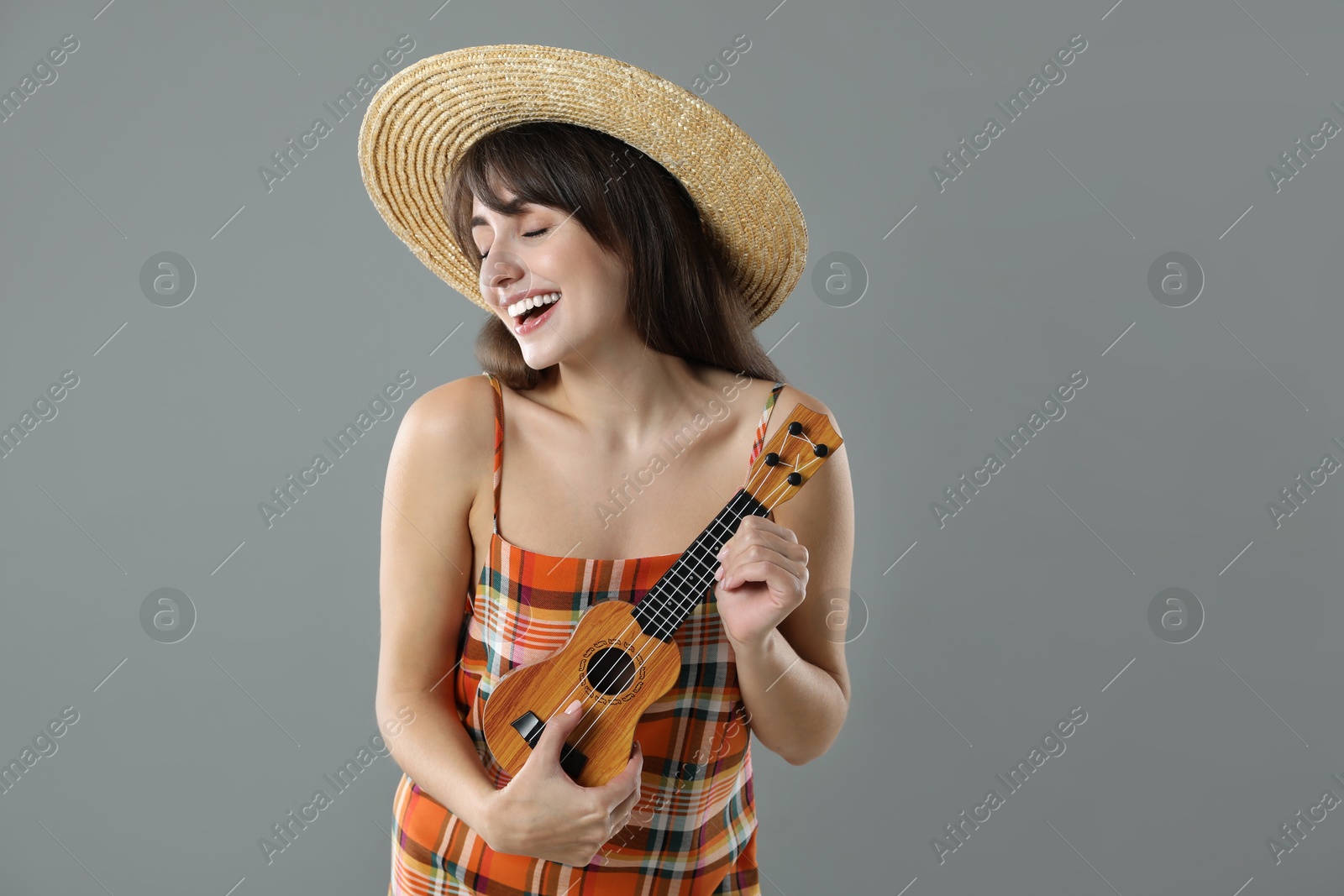 Photo of Happy woman playing ukulele on grey background