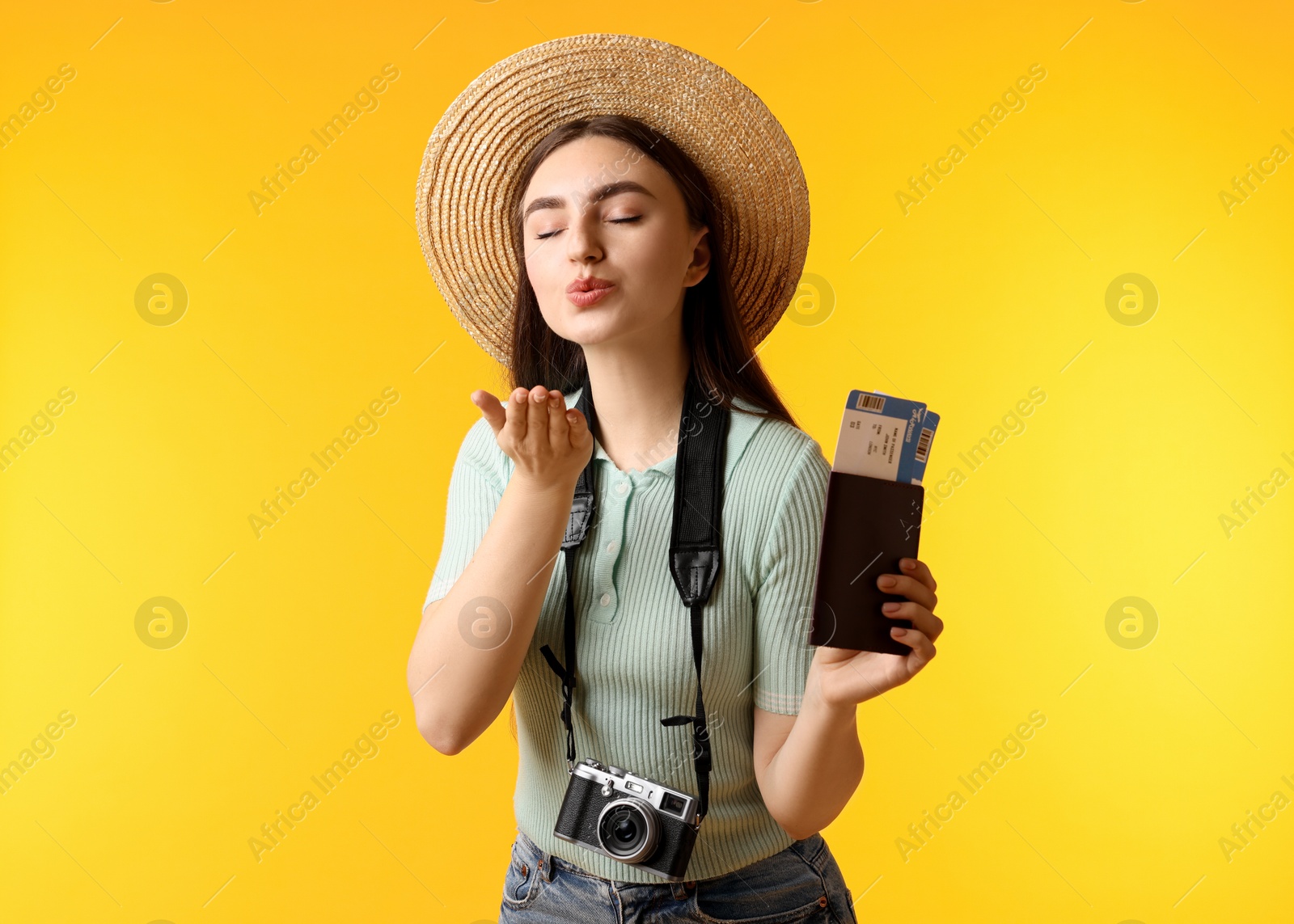 Photo of Woman with tickets, passport and vintage camera blowing kiss on orange background