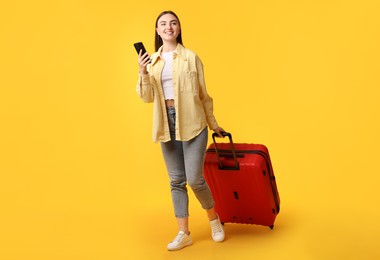 Photo of Happy woman with suitcase and smartphone on orange background