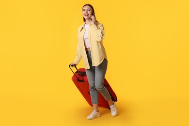 Photo of Happy woman with suitcase talking on smartphone against orange background