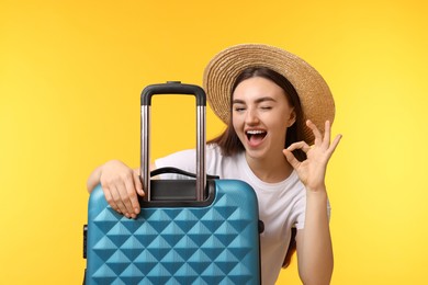 Photo of Woman in straw hat with suitcase showing ok gesture on orange background