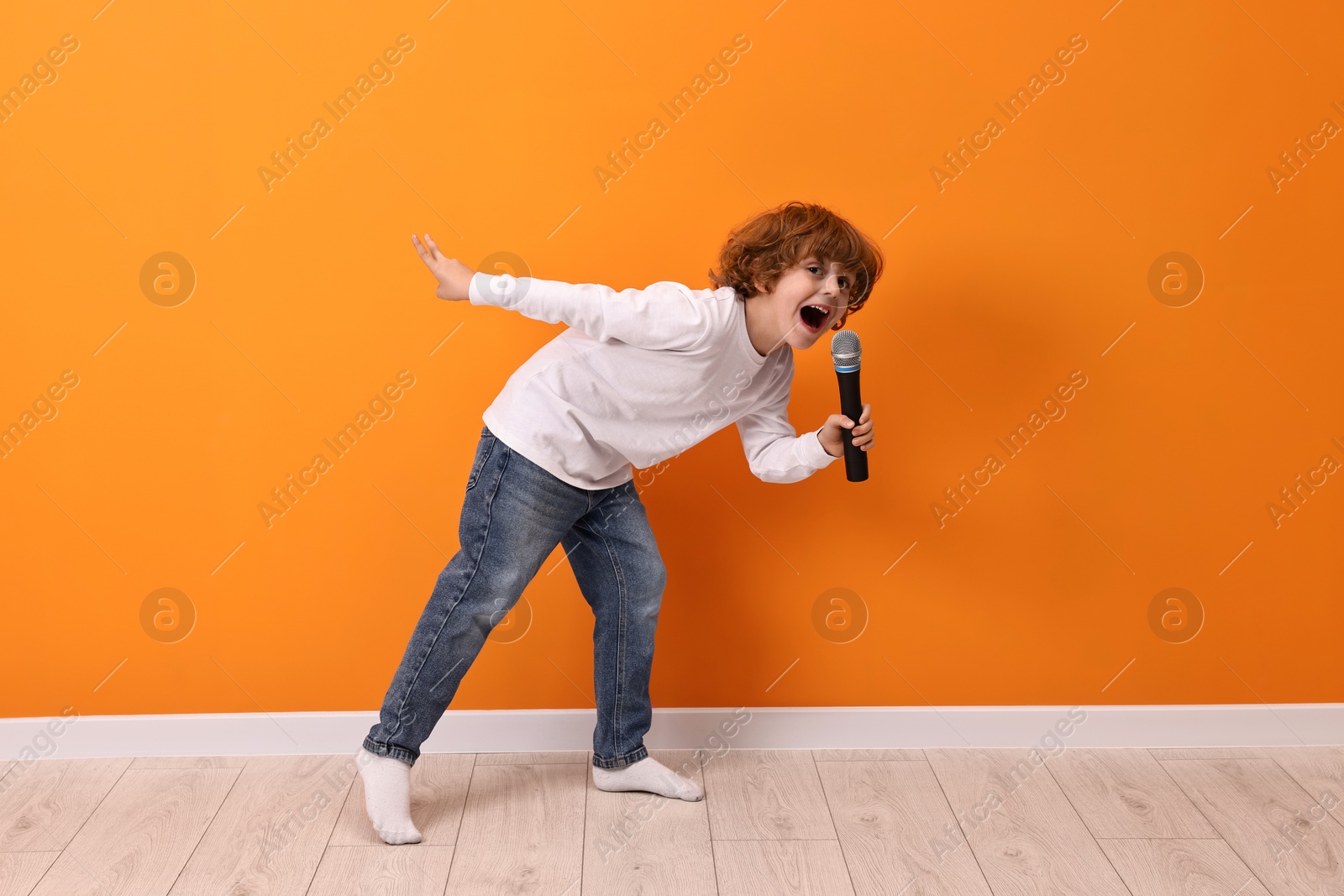 Photo of Little boy with microphone singing near orange wall