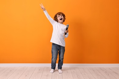 Photo of Little boy with microphone singing near orange wall