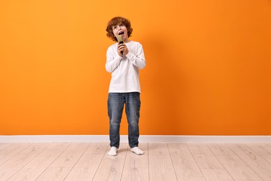 Photo of Little boy with microphone singing near orange wall