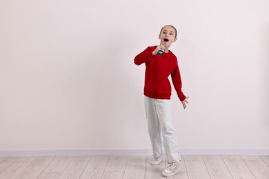 Photo of Little girl with microphone singing near white wall. Space for text