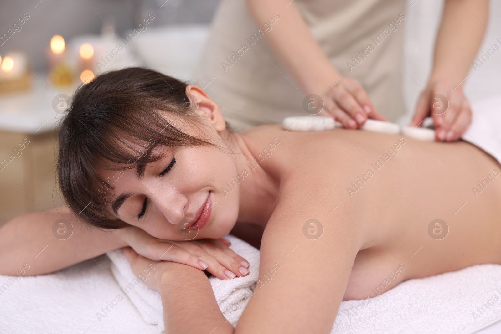 Photo of Young woman receiving hot stone massage in spa salon