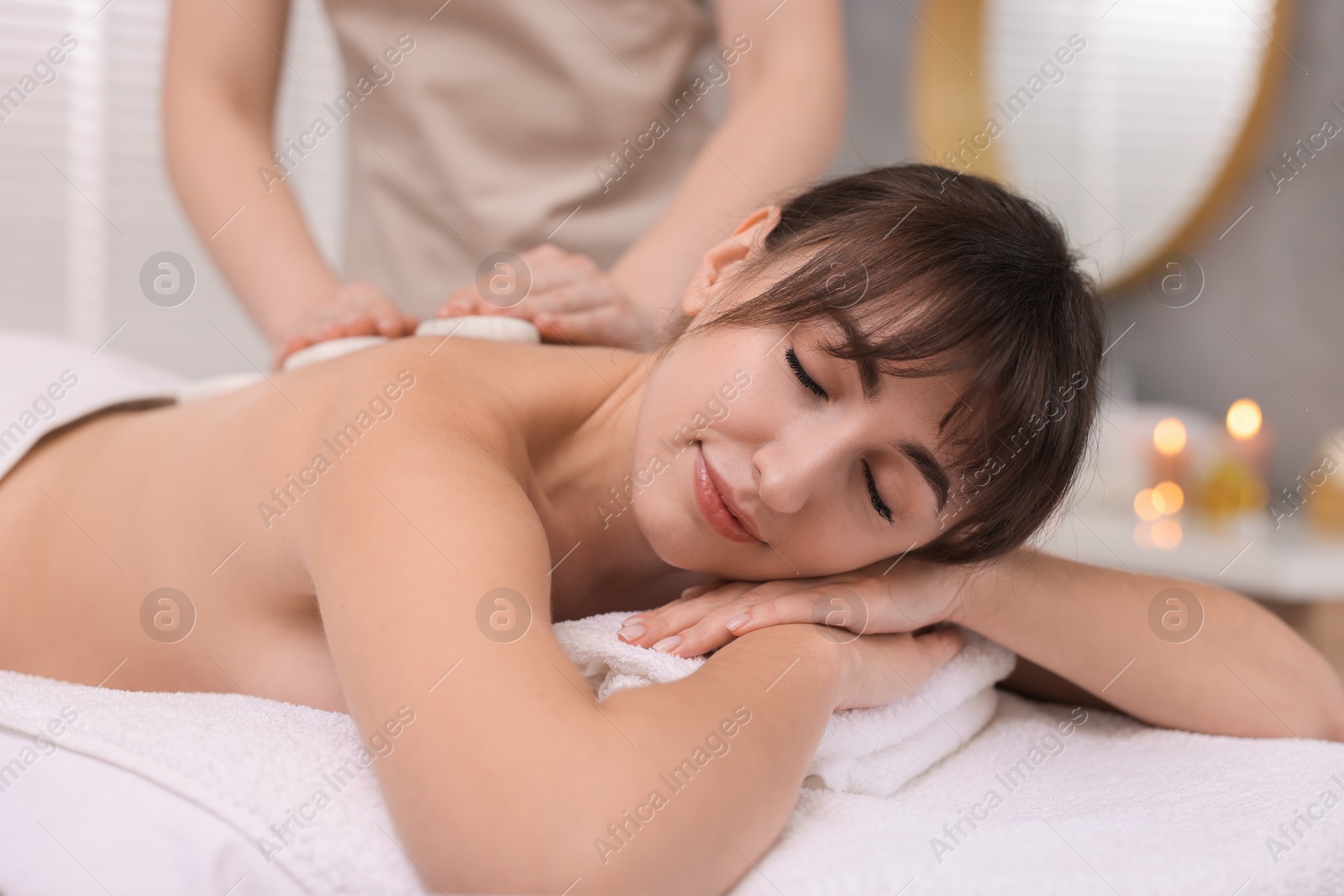 Photo of Young woman receiving hot stone massage in spa salon