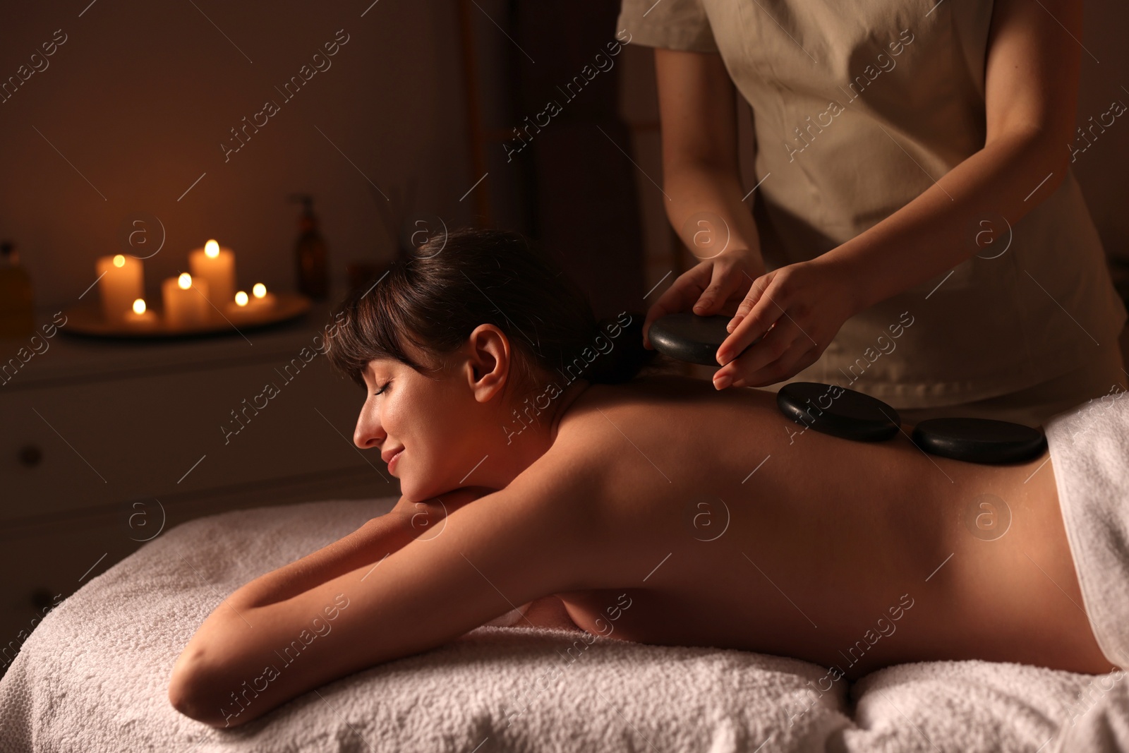 Photo of Young woman receiving hot stone massage in spa salon